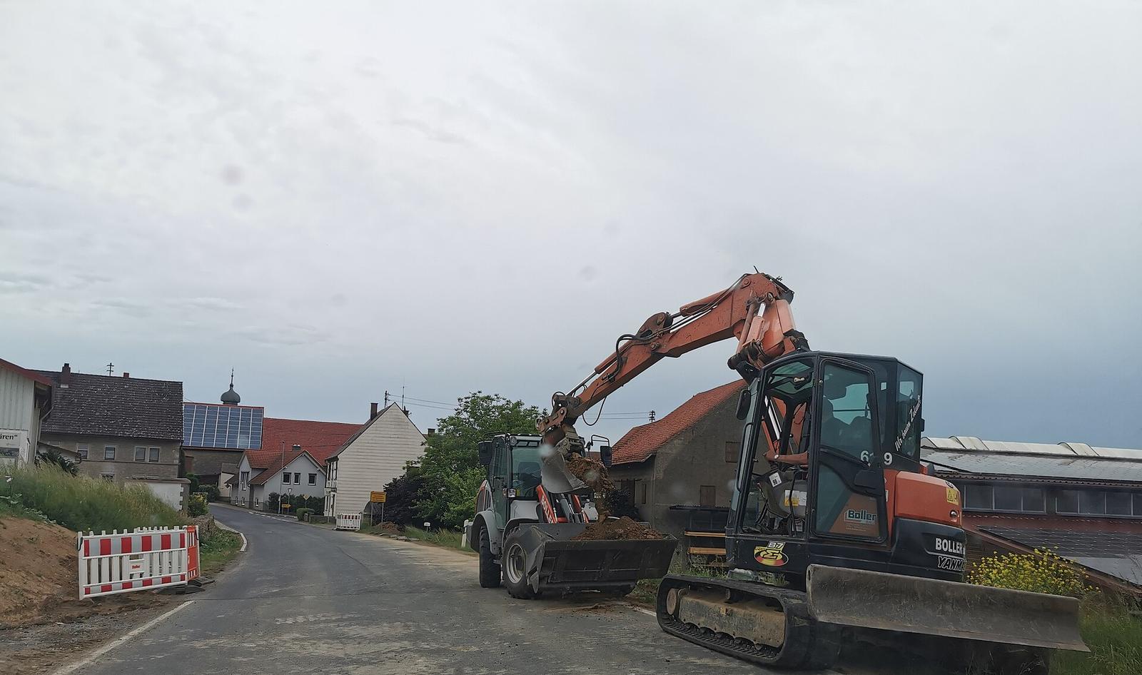 Een graafmachine en een kraan aan het werk langs een dorpsstraat